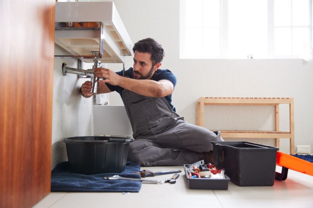 Male plumber sitting on the floor fixing a leaking sink.