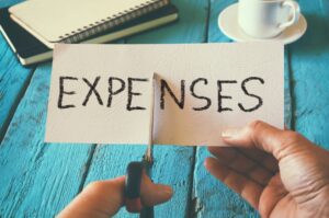 Photo of the word expenses written on paper being cut in half by hands with scissors.