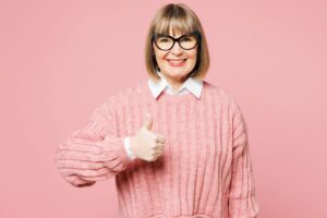 Elderly smiling happy fun customer wearing a pink sweater posing with her thumb up. 