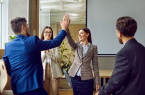 Smiling female employee dressed smart high fiving male colleague.