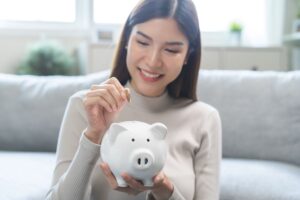 Smiling asian female saving money putting a coin in a piggy bank. 