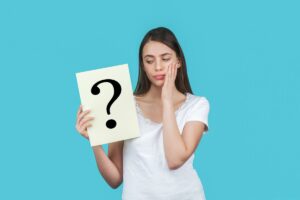 Young brunetted female on a blue background holding a card with a question mark.