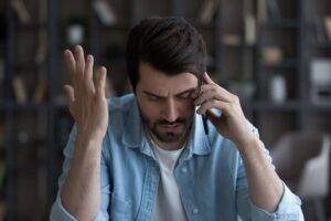 Disgruntled businessman sitting at desk with his mobile phone to his ear.