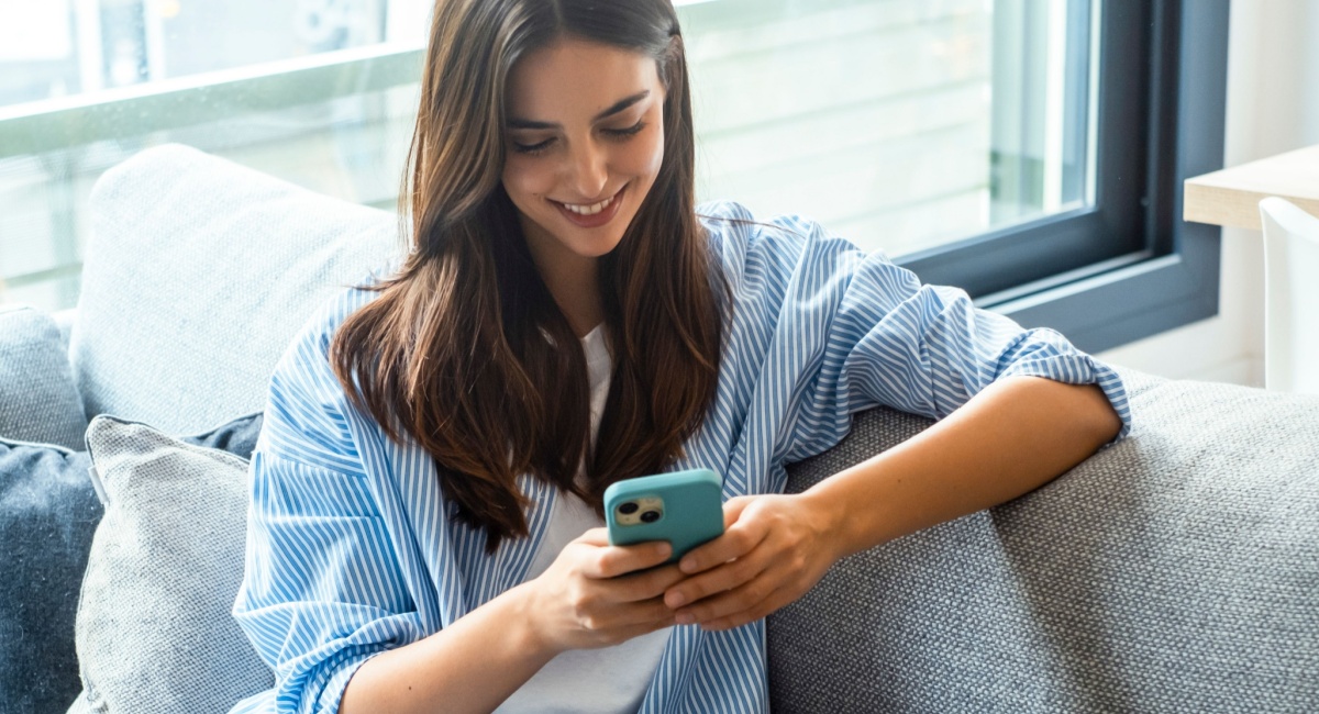 A woman seated on a couch, focused on her phone, showcasing her commitment to customer service excellence.