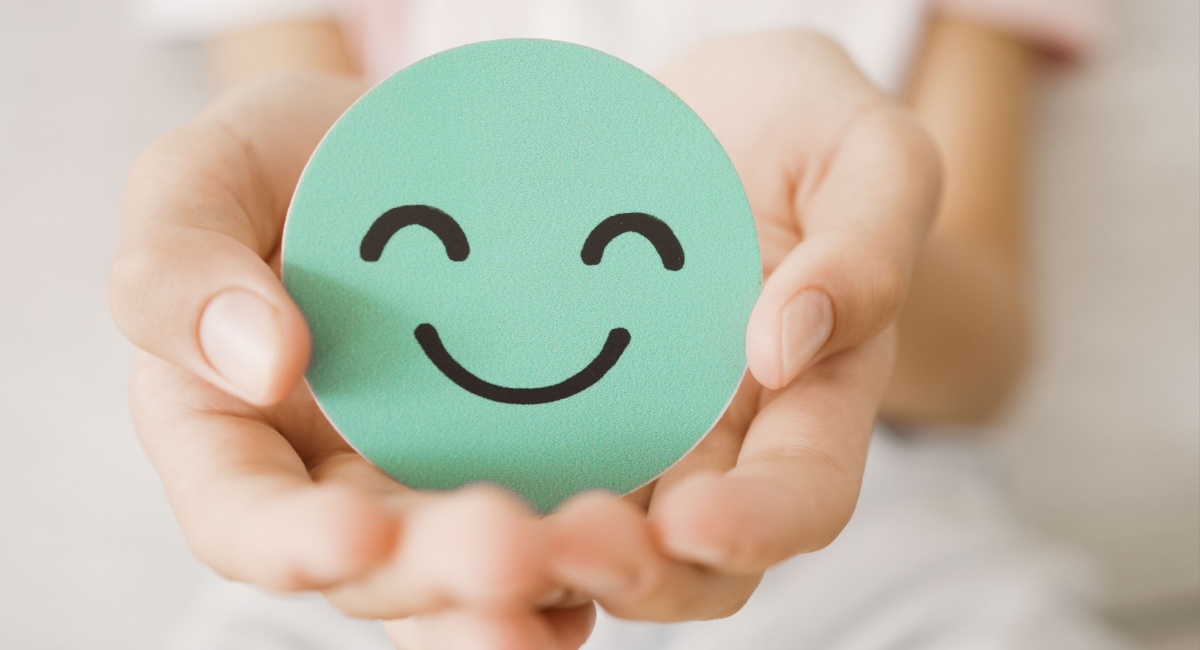 Hands holding a green smiley face sticker, symbolising customer service excellence and positivity.