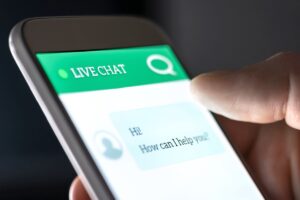 A hand using Live Chat on a Smartphone with the message displayed 'Hi! How can I help you?'