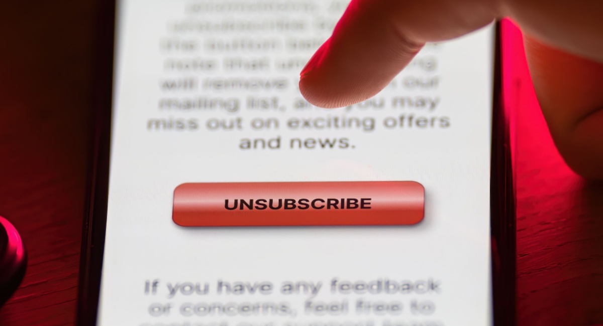 A thumb hovering over a large red 'unsubscribe' button on a phone.